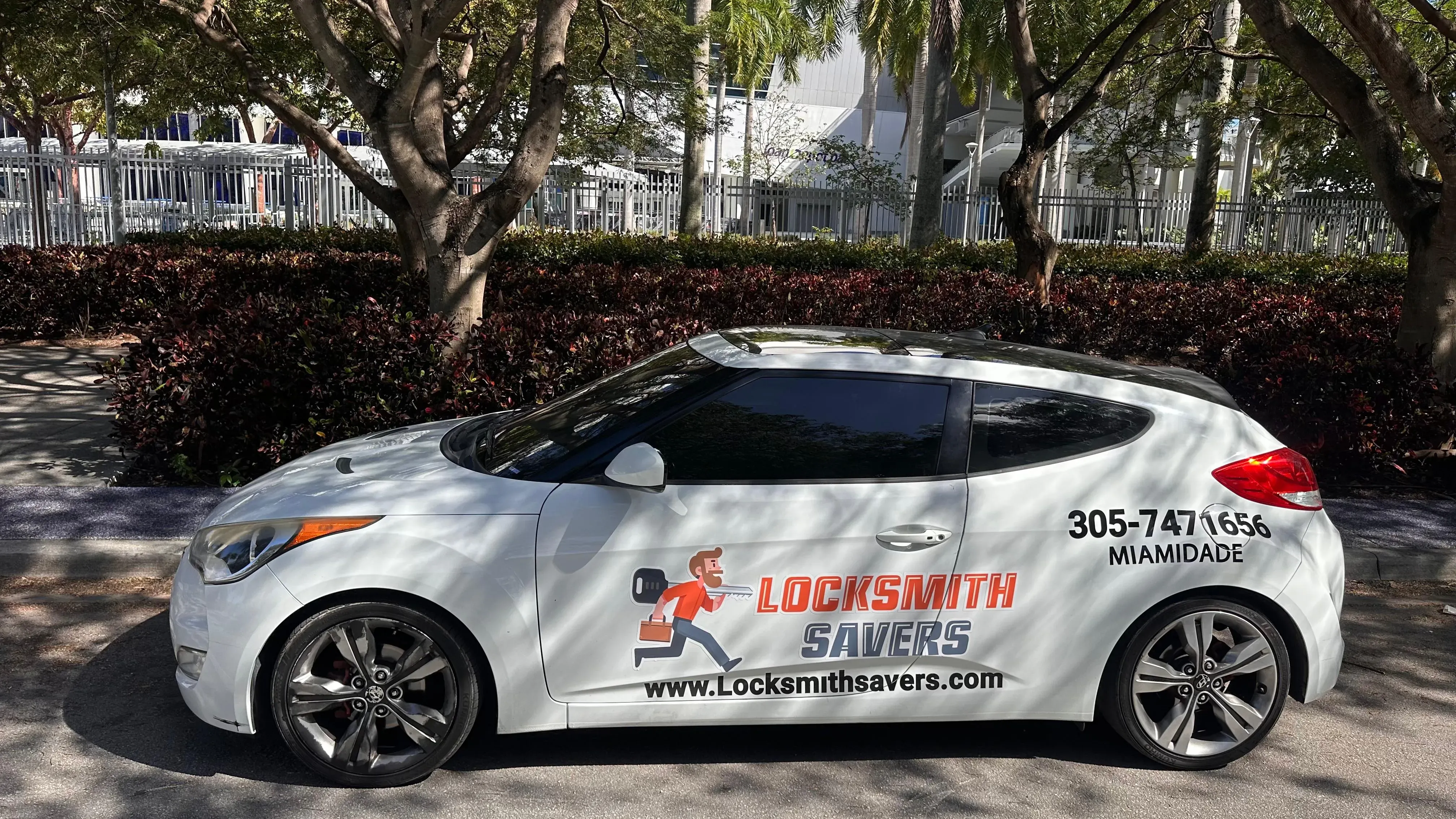 White car with Locksmith Savers branding parked under trees, representing our Miami-Dade mobile service fleet.